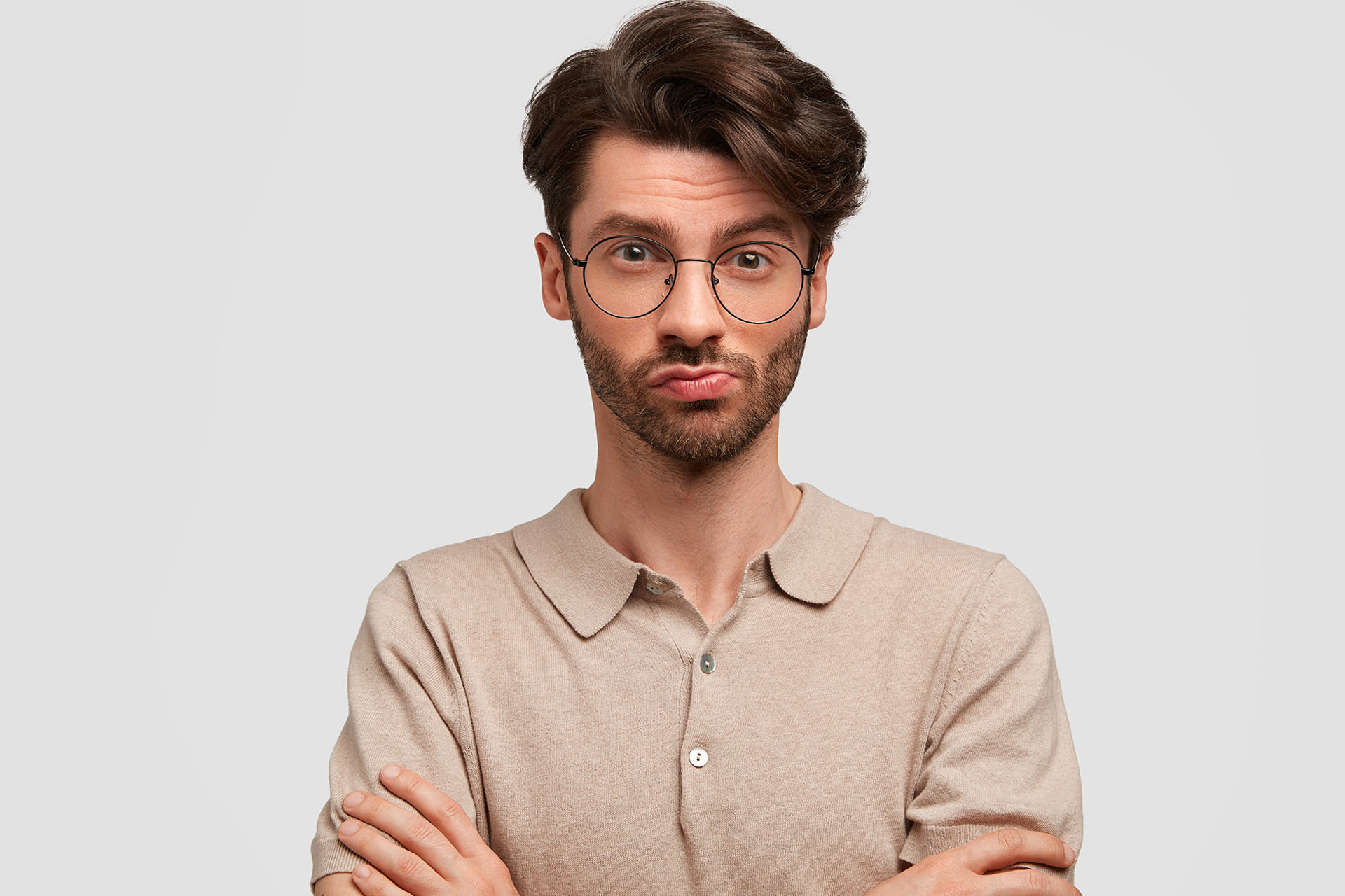 Pleased attractive overjoyed male with stubble, clenches fists, wears casual t shirt and spetalces, being in good mood, blink eyes, expresses positive emotions, isolated on white background.